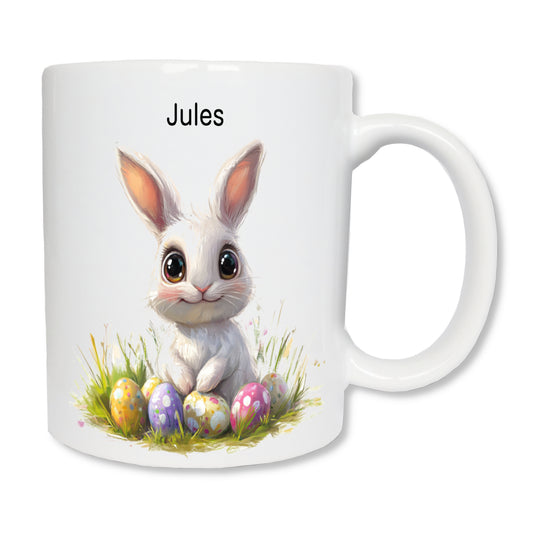 Mug blanc en céramique de 325 ml représentant un lapin de pâques blanc avec des oeufs colorés et personnalisé avec un prénom.