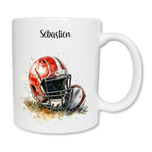 Mug blanc en céramique  de 325 ml avec le dessin d'un casque rouge et d'un ballon de rugby posé  sur de l'herbe, et personnalisé avec un prénom. Un cadeau pour rugbyman ou coach.