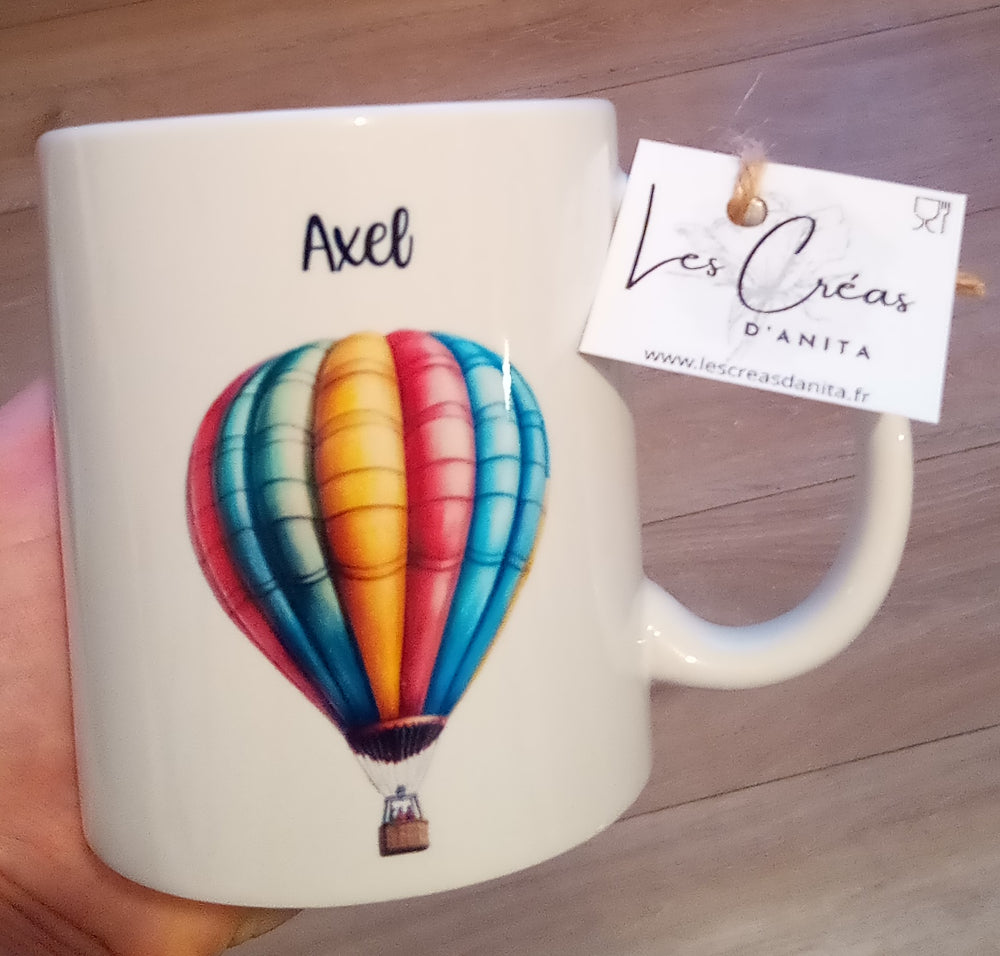 Mug blanc en céramique de 325 ml avec une montgolfière multicolore et personnalisé avec un prénom. Idée cadeau idéal pour anniversaire enfant