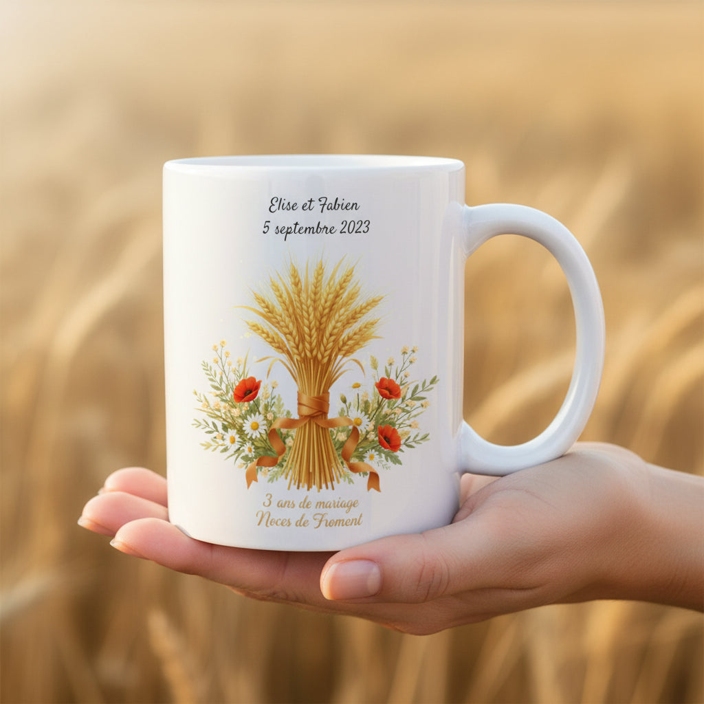 Mug personnalisé 3 ans de mariage Noces de Froment, tenu dans une main avec illustration gerbe de blé et coquelicots sur fond de champ doré

