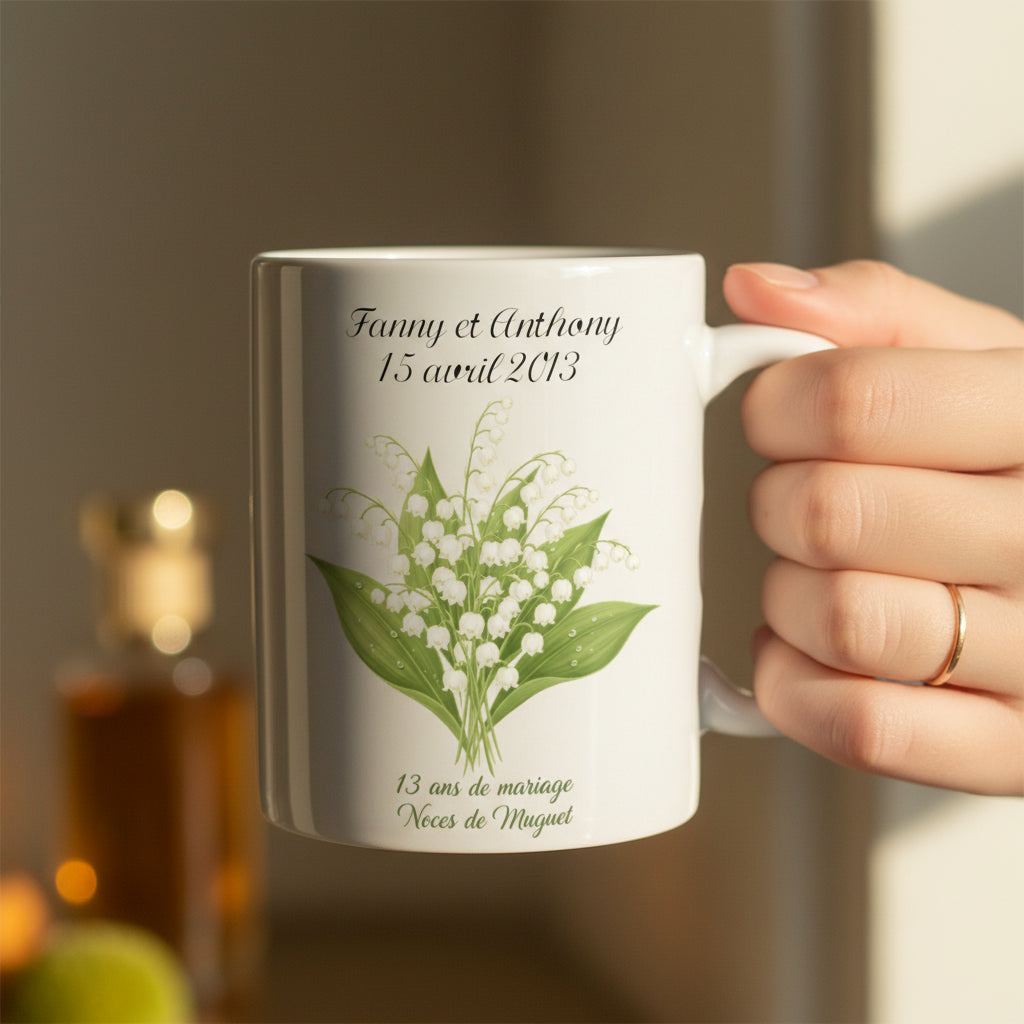 Mug personnalisé 13 ans de mariage Noces de Muguet, tenu à la main avec illustration bouquet de muguet blanc sur fond doux ambré

