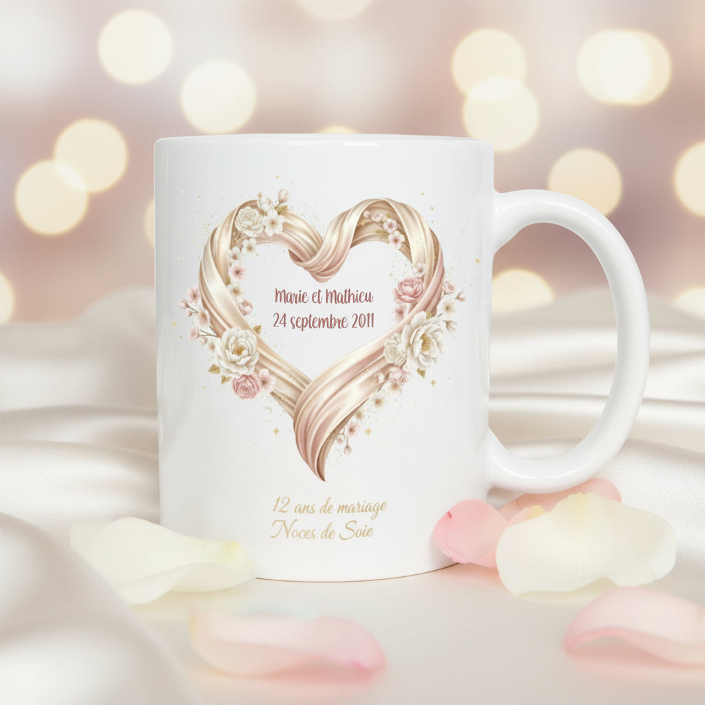 Mug personnalisé 12 ans de mariage Noces de Soie, posé sur un tissu de soie blanc avec pétales roses et bokeh lumineux, illustration cœur en ruban de soie doré et fleurs

