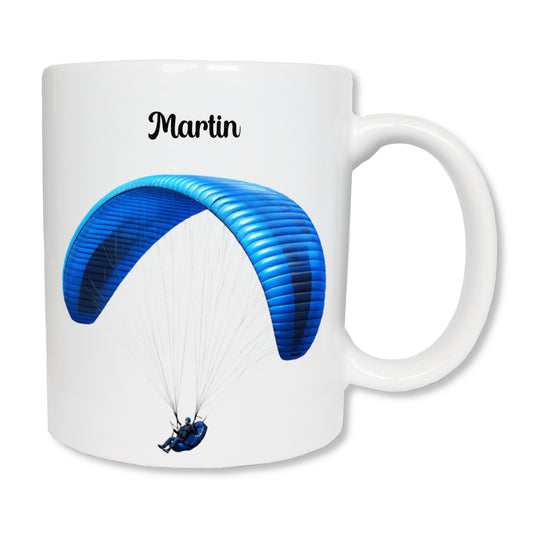 Mug blanc en céramique de 325 ml avec le dessin représentant un homme qui fait du parapente de couleur bleue, et personnalisé avec un prénom. Cadeau pour parapentiste.