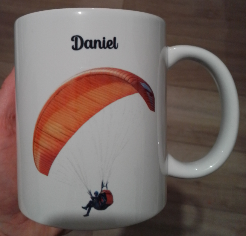 Mug blanc en céramique 325 ml avec le dessin représentant un homme qui fait du parapente de couleur orange, et personnalisé avec un prénom. Cadeau  anniversaire parapentiste.