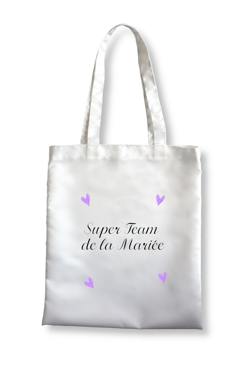 Tote bag personnalisé blanc en polyester affichant le texte "Super Team de la Mariée" et quatre coeurs roses autour